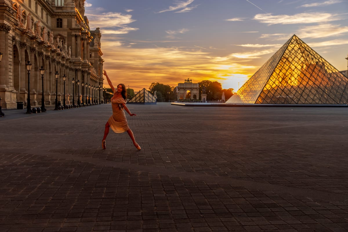 A ballerina in an orange dress leaping across the empty courtyard of the Louvre, the glass pyramid catching the last light behind her.