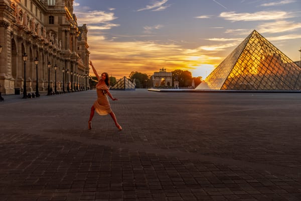 A ballerina in an orange dress leaping across the empty courtyard of the Louvre, the glass pyramid catching the last light behind her.