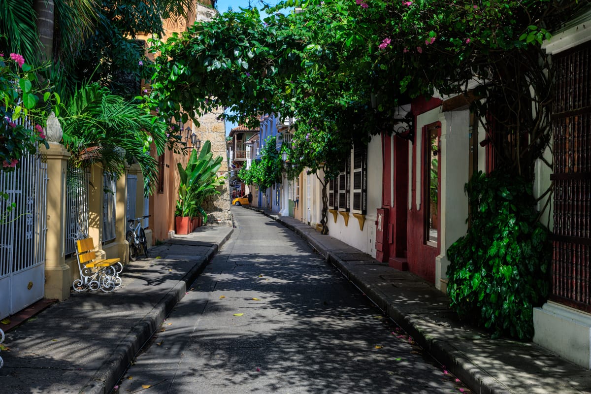 A narrow street in the old town of Cartagena lined with pastel houses, hung with green creepers and empty of traffic in the early afternoon.