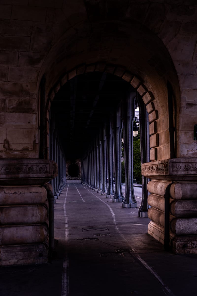 The lower deck of the Pont de Bir-Hakeim in Paris, a long stone arcade of paired columns receding into shadow.